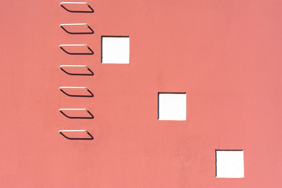 Minimalist pink building facade featuring a stark white ladder and geometric windows.