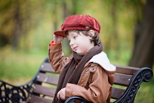Boy Wearing Red Beret Cap While Sitting on Bench
