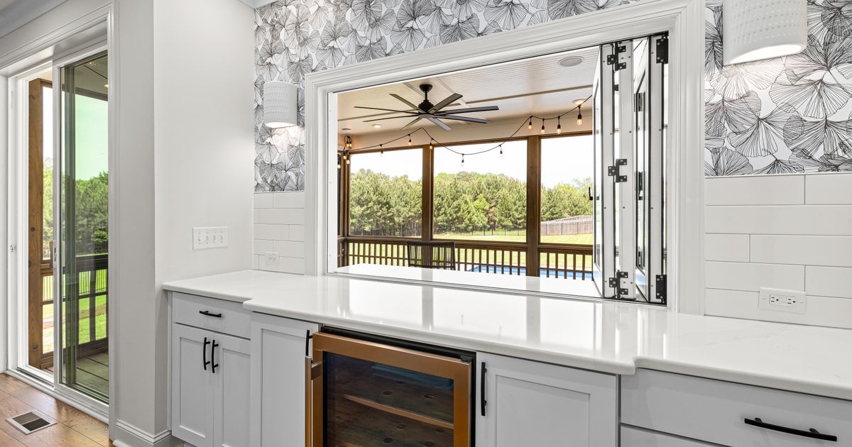 Bright white kitchen with an under-counter glass-door wine cooler below the worktop and a serving hatch open onto a covered porch