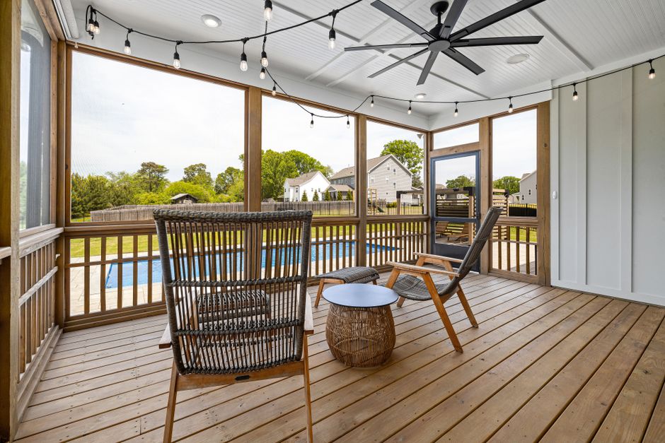 Stylish screened terrace with wooden furniture and ceiling fan, overlooking a serene backyard pool.
