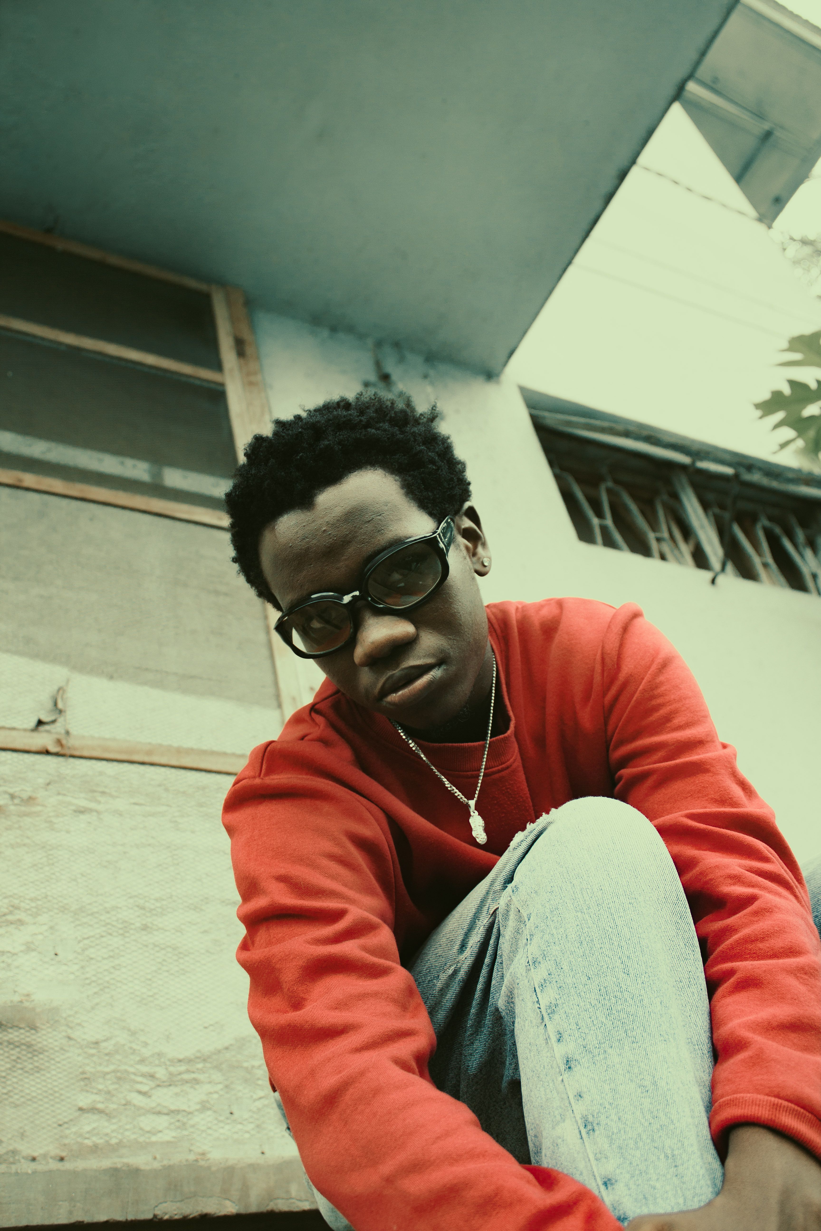 Portrait of an adult man wearing eyeglasses and a red sweatshirt sitting outdoors.