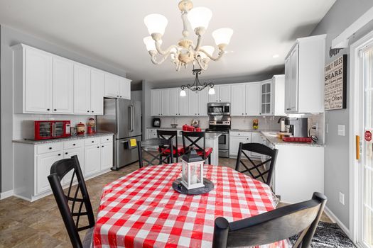 Bright modern kitchen with red accents and white cabinetry around a checkered dining table.
