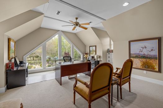 A well-lit home office space with stylish furniture, large windows overlooking the garden, and elegant decor.