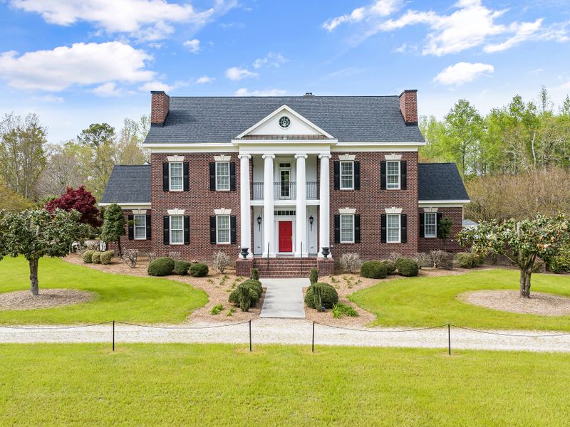 Colonial-style brick residence with pillars and a lush front garden