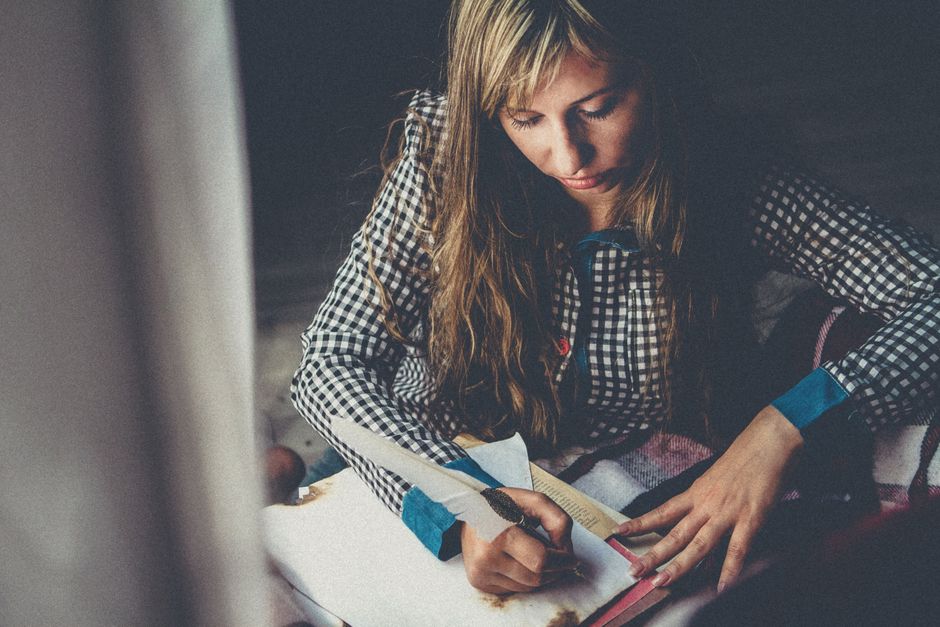 Blonde woman writing with feather quill at home, creating an artistic and cozy atmosphere.