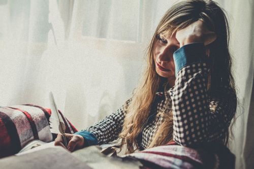 Free A woman with a quill, deep in thought by a sunlit window, in a plaid shirt. Stock Photo