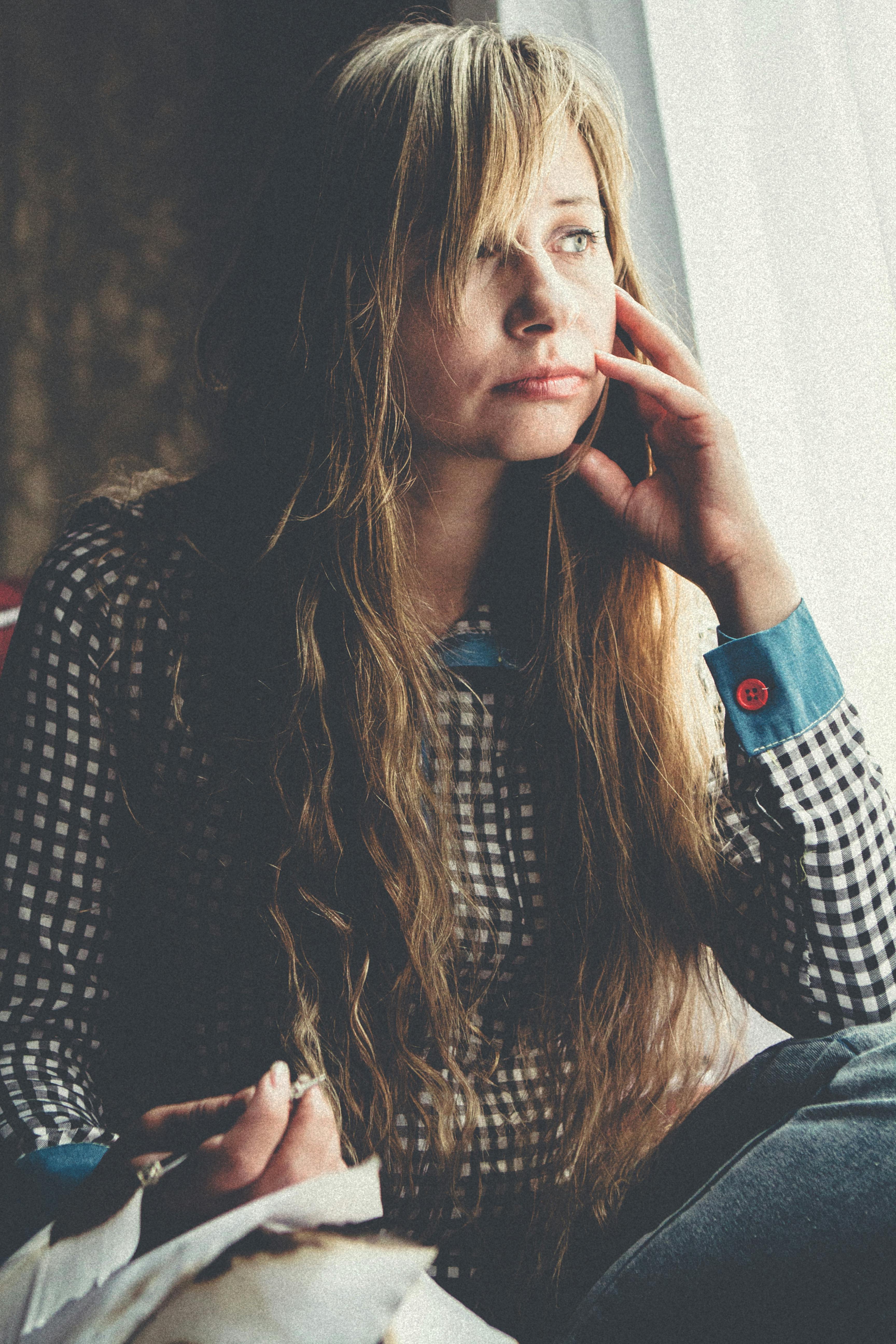 Thoughtful woman gazes outside while sitting indoors in natural light.