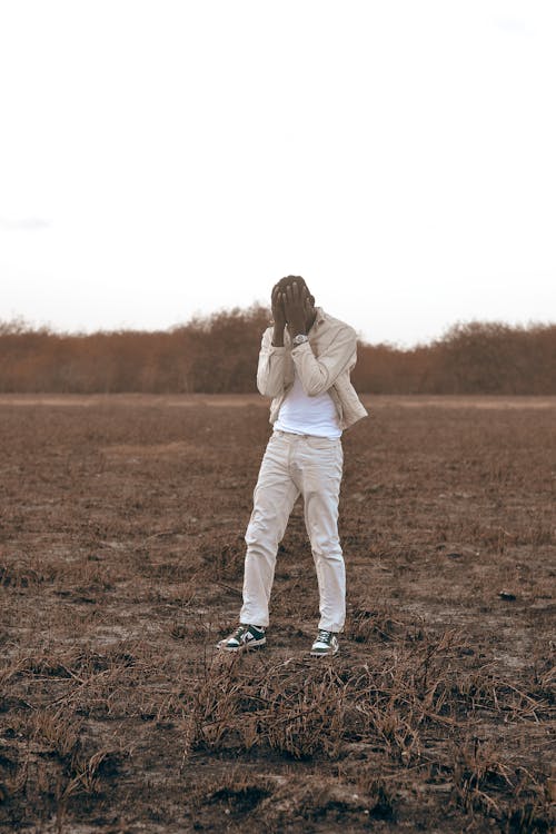 Man Wearing Bright Clothing Standing in a Muddy Field and Covering His Face in Hands