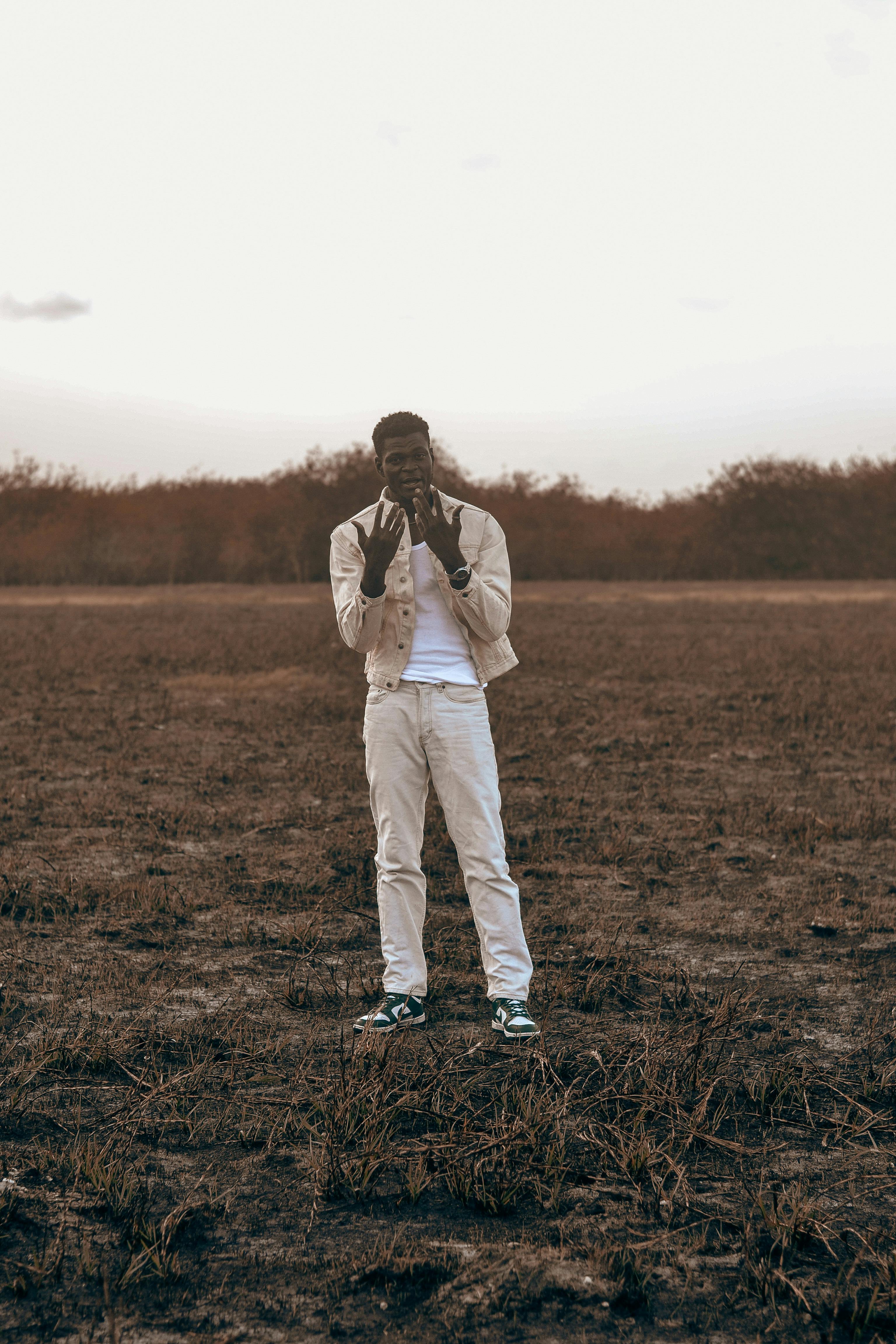 A young man in bright clothing stands in a field near Accra, Ghana during sunset.