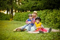 在一个阳光明媚的夏日下午，母亲和两个儿子在公园里铺着毯子，悠闲地放松