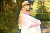 一位戴着帽子、披着披肩的长卷发妇女，在晴朗的午后享受户外时光