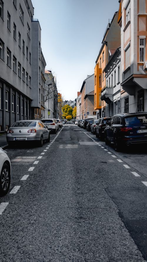 Free A vertical shot of a city street lined with parked cars and residential buildings, showcasing urban symmetry. Stock Photo