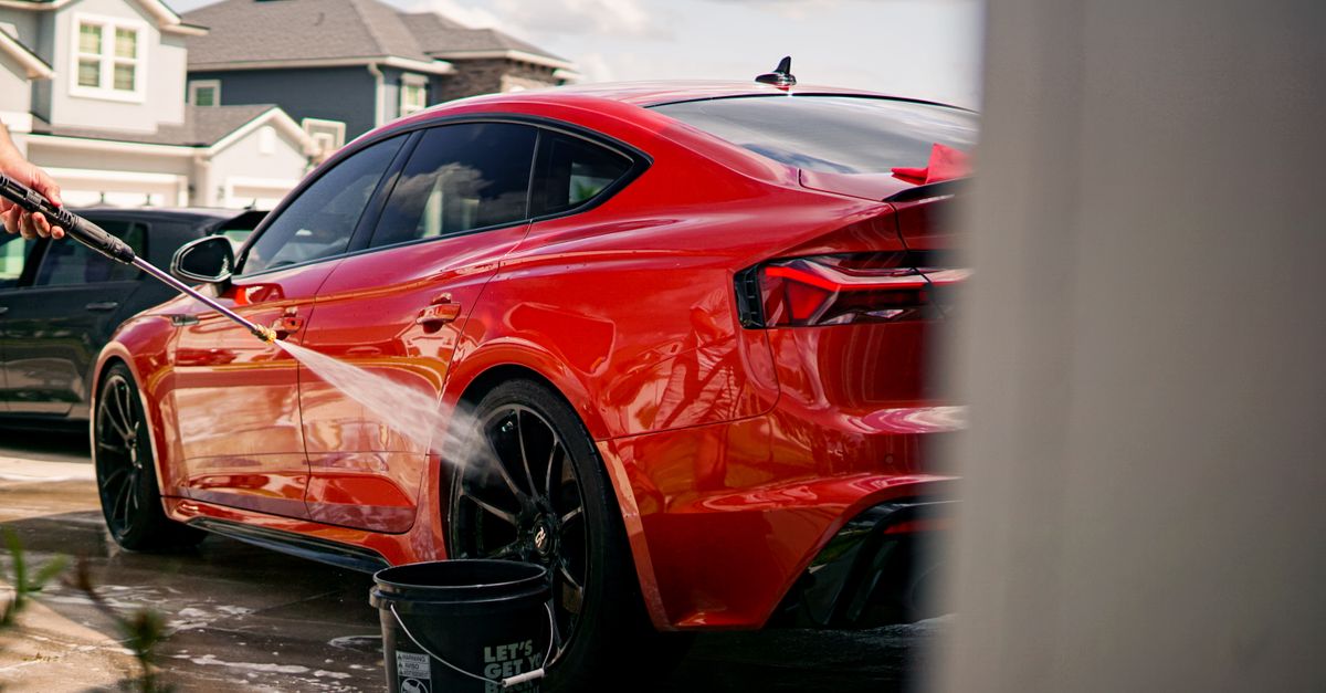 A vibrant red luxury car being washed outdoors in a suburban residential area.