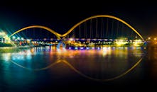 一座明亮的现代吊桥在夜间呈现出令人惊叹的景象，水面上倒映着缤纷的色彩