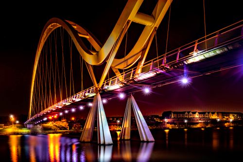 Free Beautiful nighttime view of a futuristic illuminated bridge reflecting on a calm river. Stock Photo