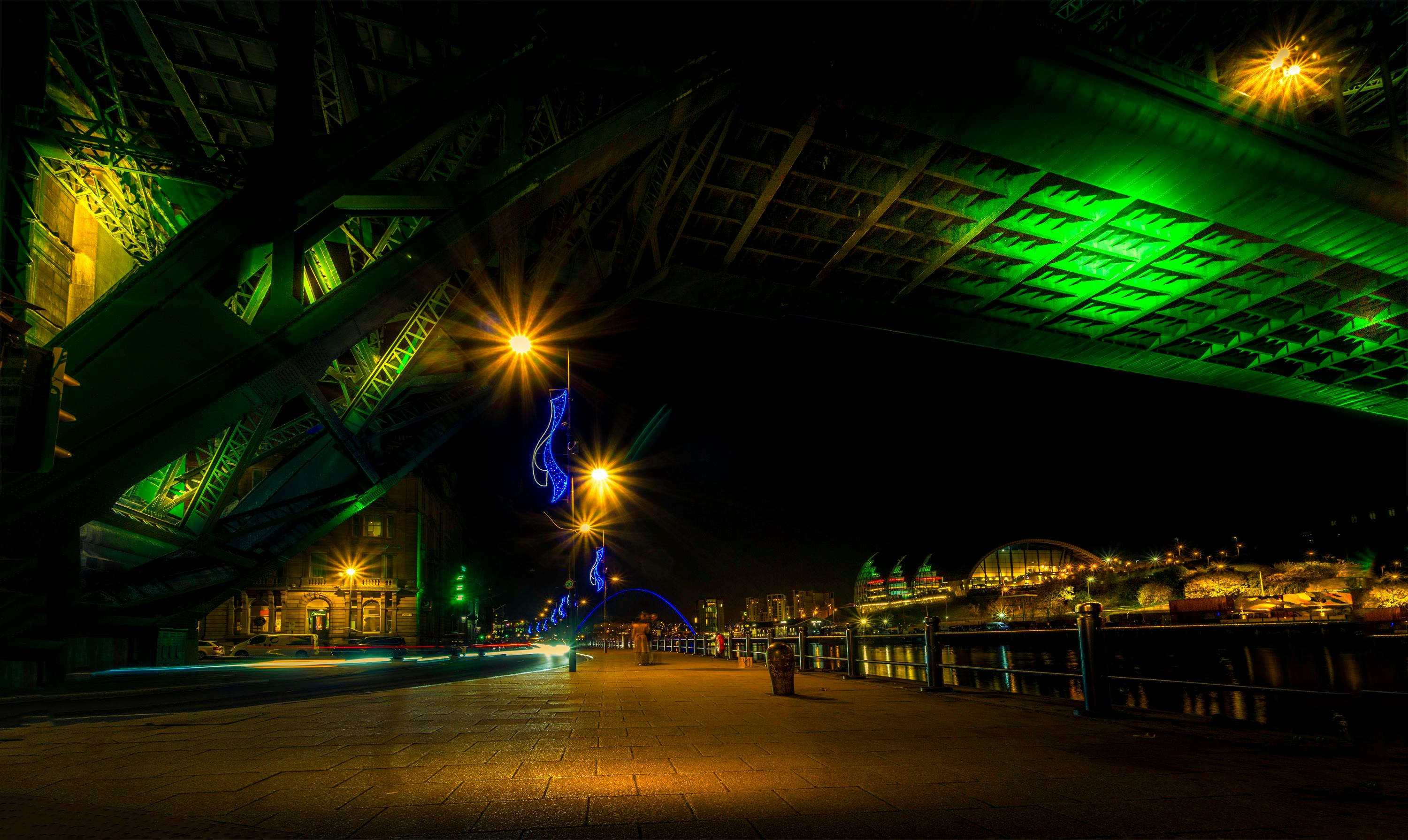 桥下绿色照明映衬着城市景观，浅色条纹的夜景显得格外生动