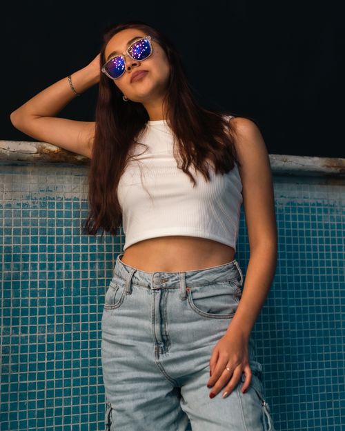 Free Young woman posing confidently in casual wear with sunglasses against a tiled background. Stock Photo