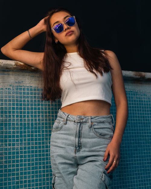 Free Young woman in casual attire and blue sunglasses posing against a tiled background. Stock Photo