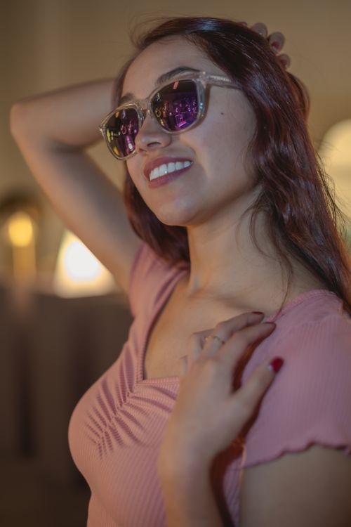Free Young woman with brown hair wearing sunglasses and a pink top indoors, smiling. Stock Photo