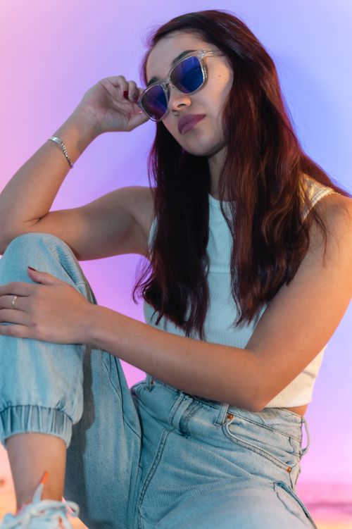 Free Fashionable young woman in casual attire posing with sunglasses against a colorful background. Stock Photo