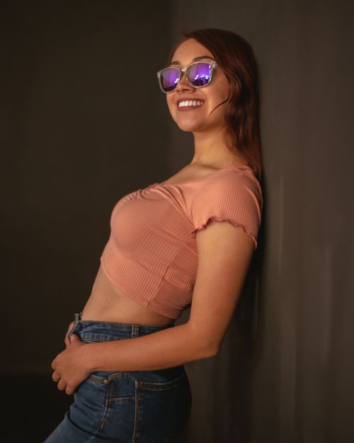 Free Fashionable young woman in a pink top, jeans, and sunglasses smiling in a studio setting. Stock Photo