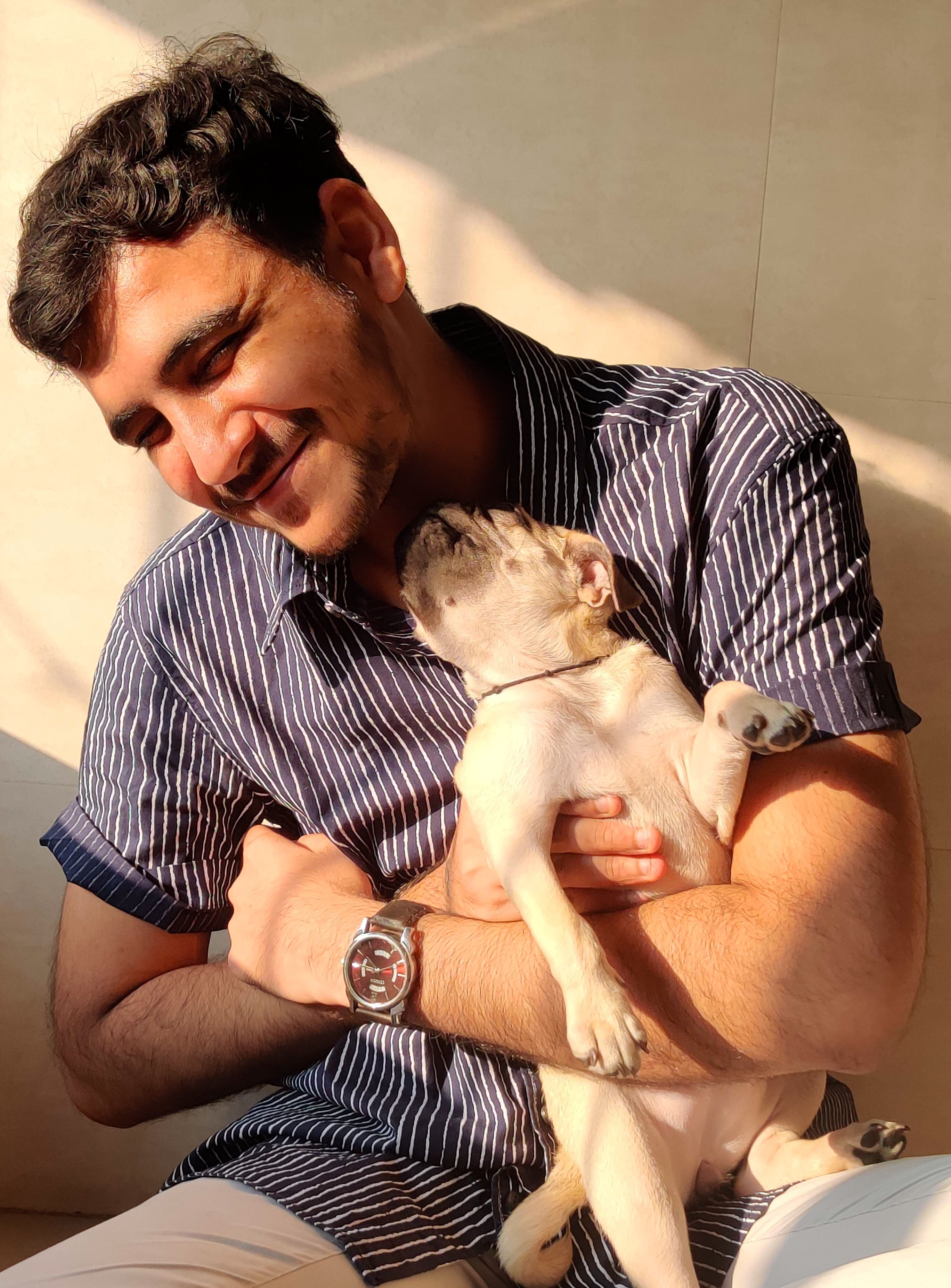 Man smiling while cuddling a French Bulldog indoors. Warm and joyful moment.