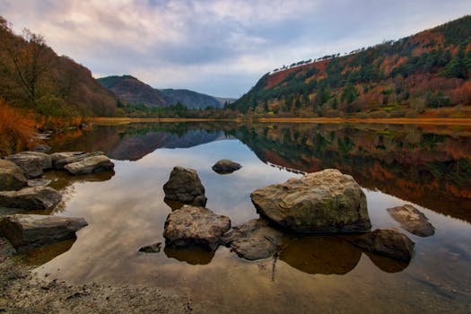 A serene early morning view at Glendalough Lake, Ireland, with stunning autumn foliage reflected in calm waters.