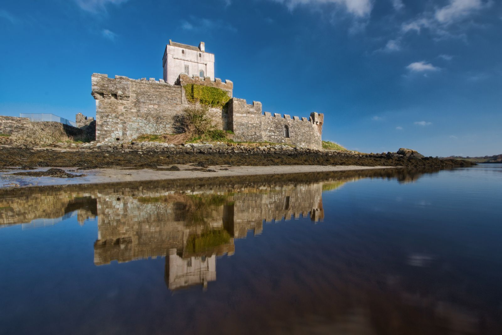 A view of Doe Castle in County Donegal, Ireland reflecting in calm waters under a clear blue sky