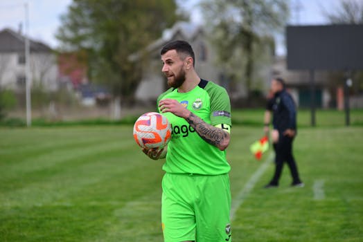 A soccer player with a beard in a green uniform is preparing for a throw-in on an outdoor field.