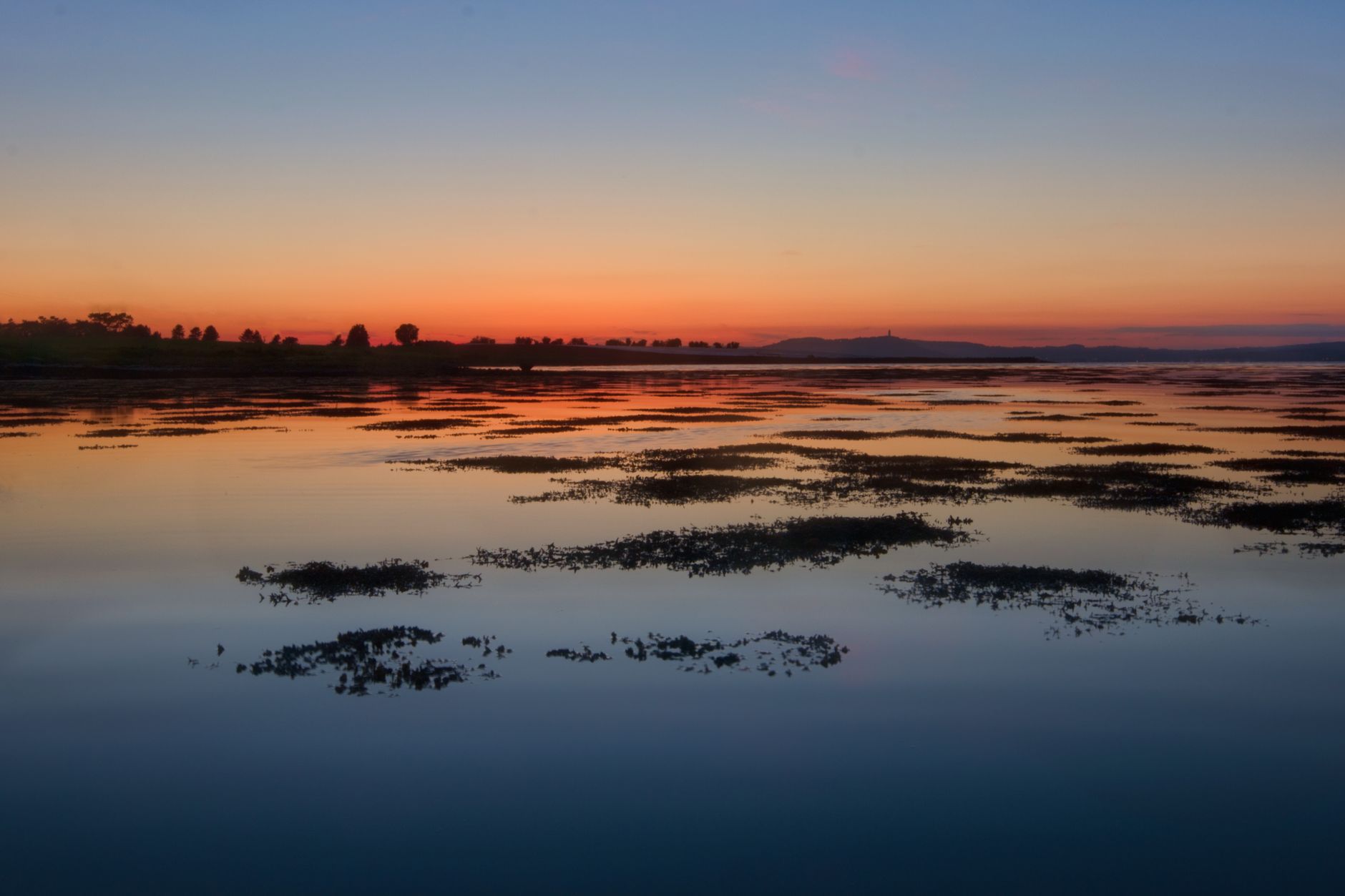 Silhouette of a serene lake reflecting a vibrant sunset in Northern Ireland