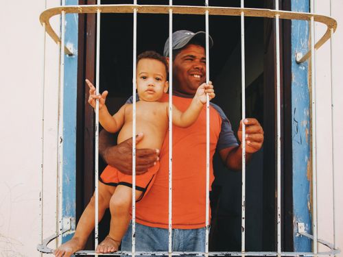 Free A father and his young son smiling and posing together through a barred window, enjoying a sunny day. Stock Photo
