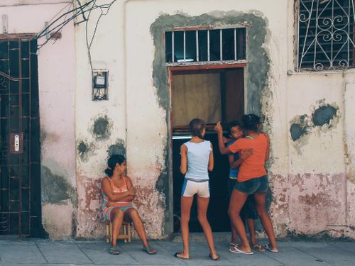 Free A candid moment of urban life with children playing and adult seated against a weathered building facade. Stock Photo