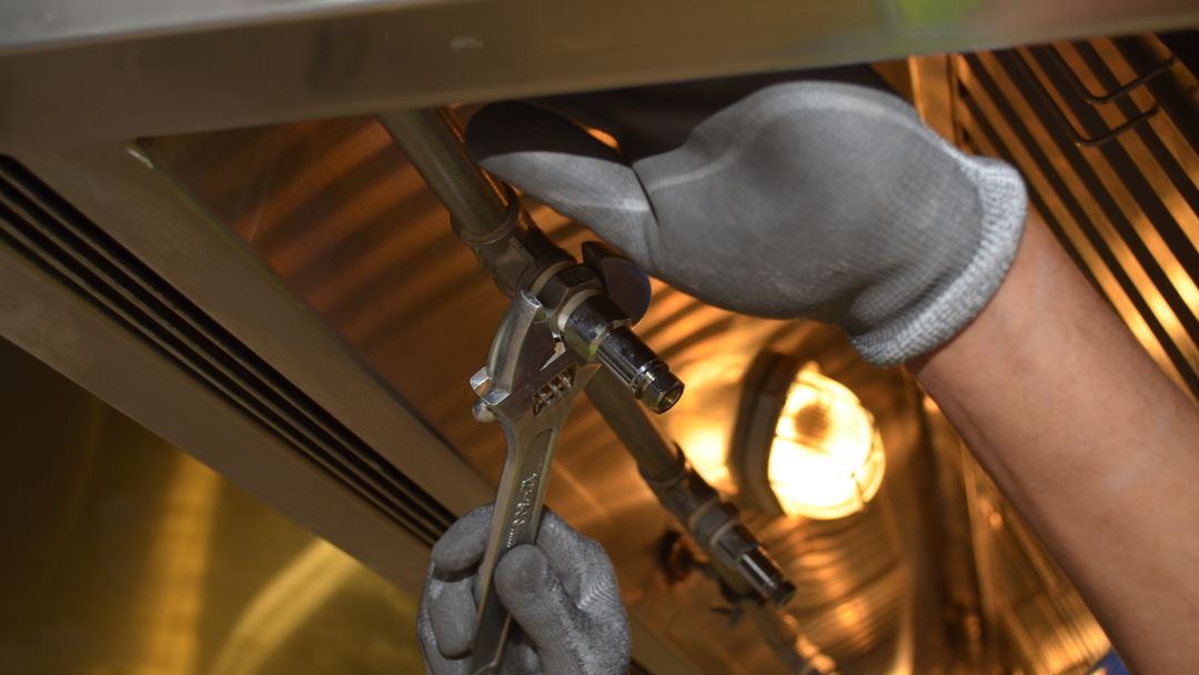 A worker tightening a pipe fitting with a spanner