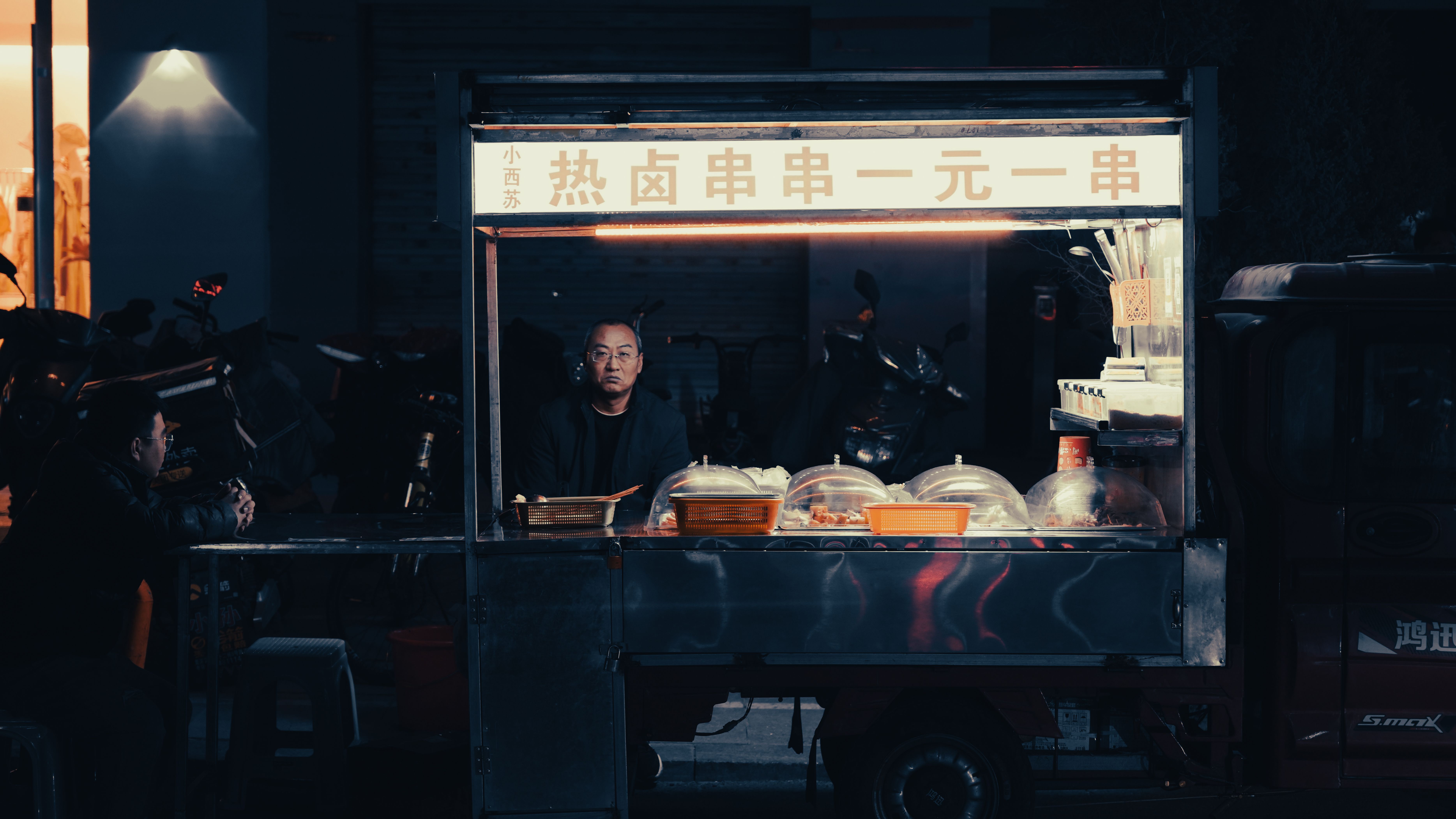 A street vendor serves traditional food at night in an illuminated urban setting.