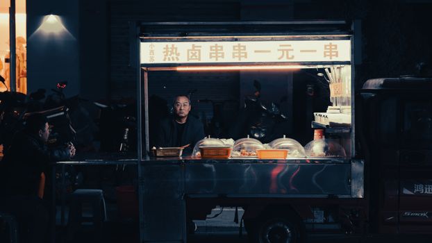 A street vendor serves traditional food at night in an illuminated urban setting.
