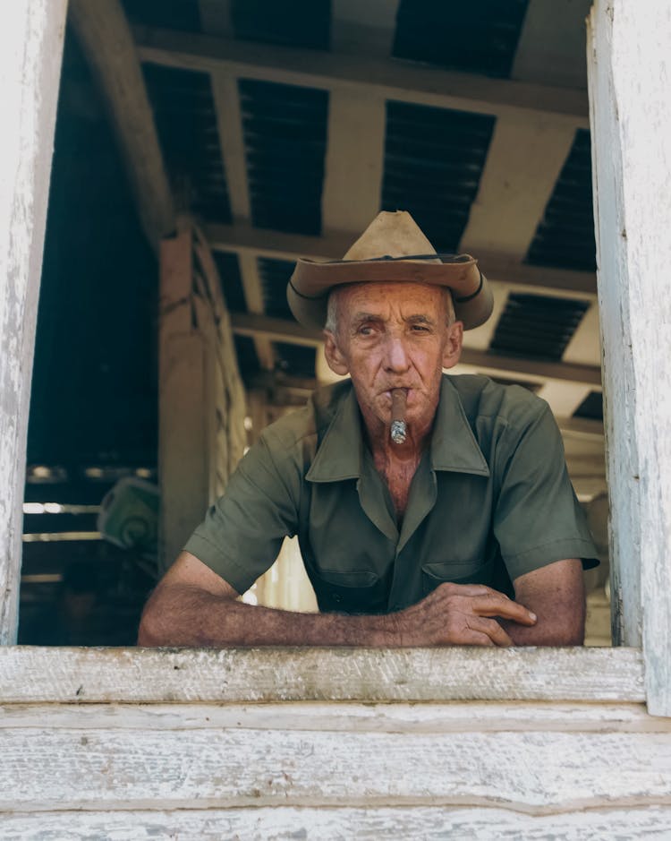 Elderly Man Looking Out The Window And Smoking A Cigar 