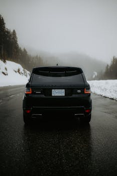 Back view of a luxury SUV on a snowy mountain road, foggy winter scene.