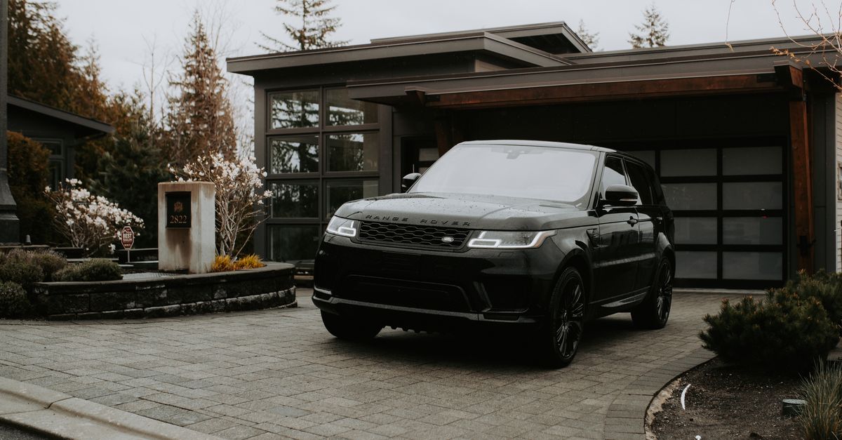 A sleek black luxury SUV parked in front of a modern home with glass facade.
