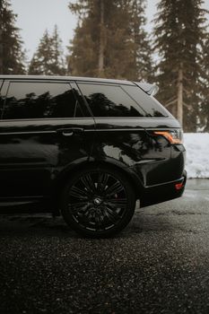 Side view of a black SUV parked on a snowy road, surrounded by winter trees.