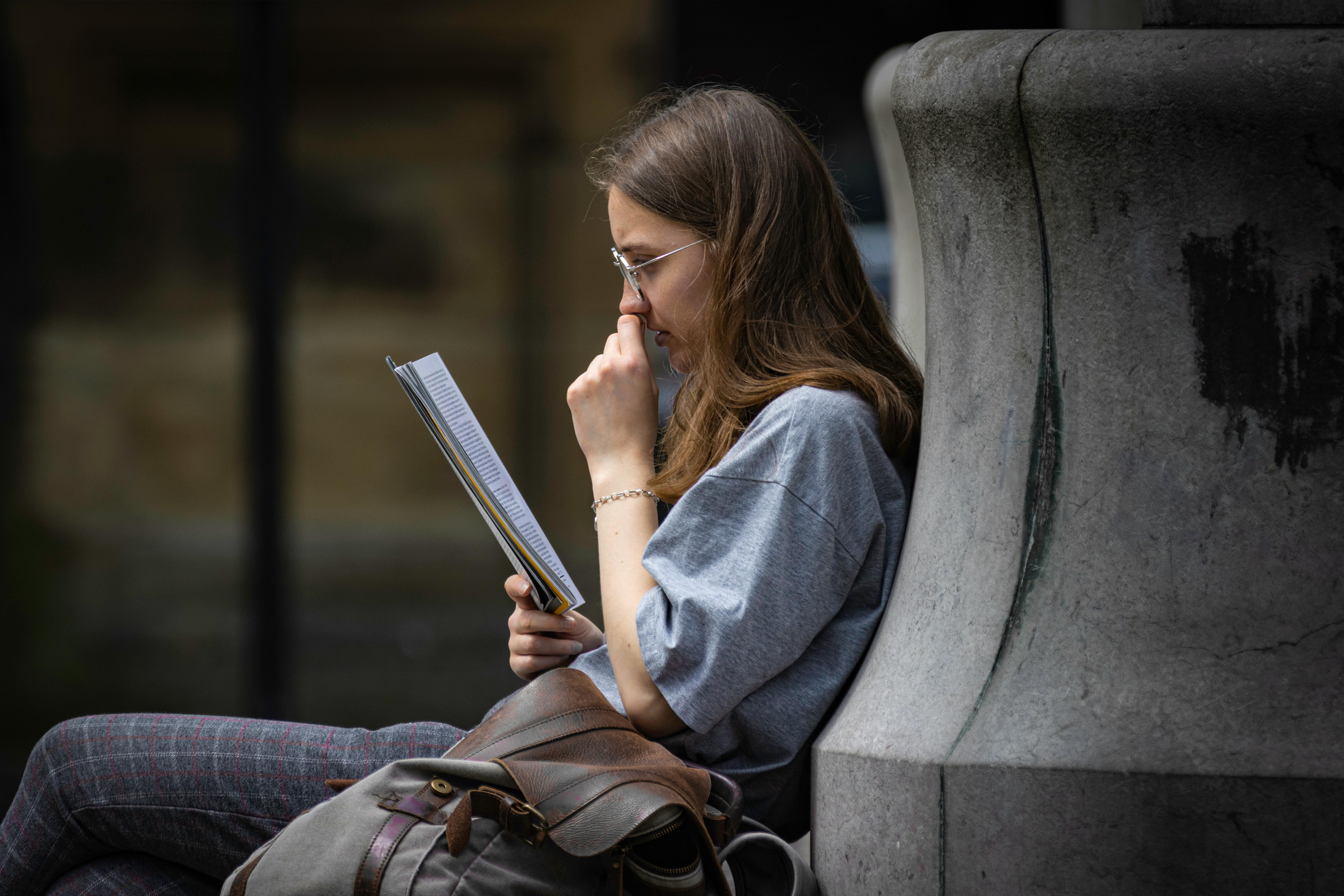 Young woman reading outdoors on a street in Lancaster, England, showcasing urban life.