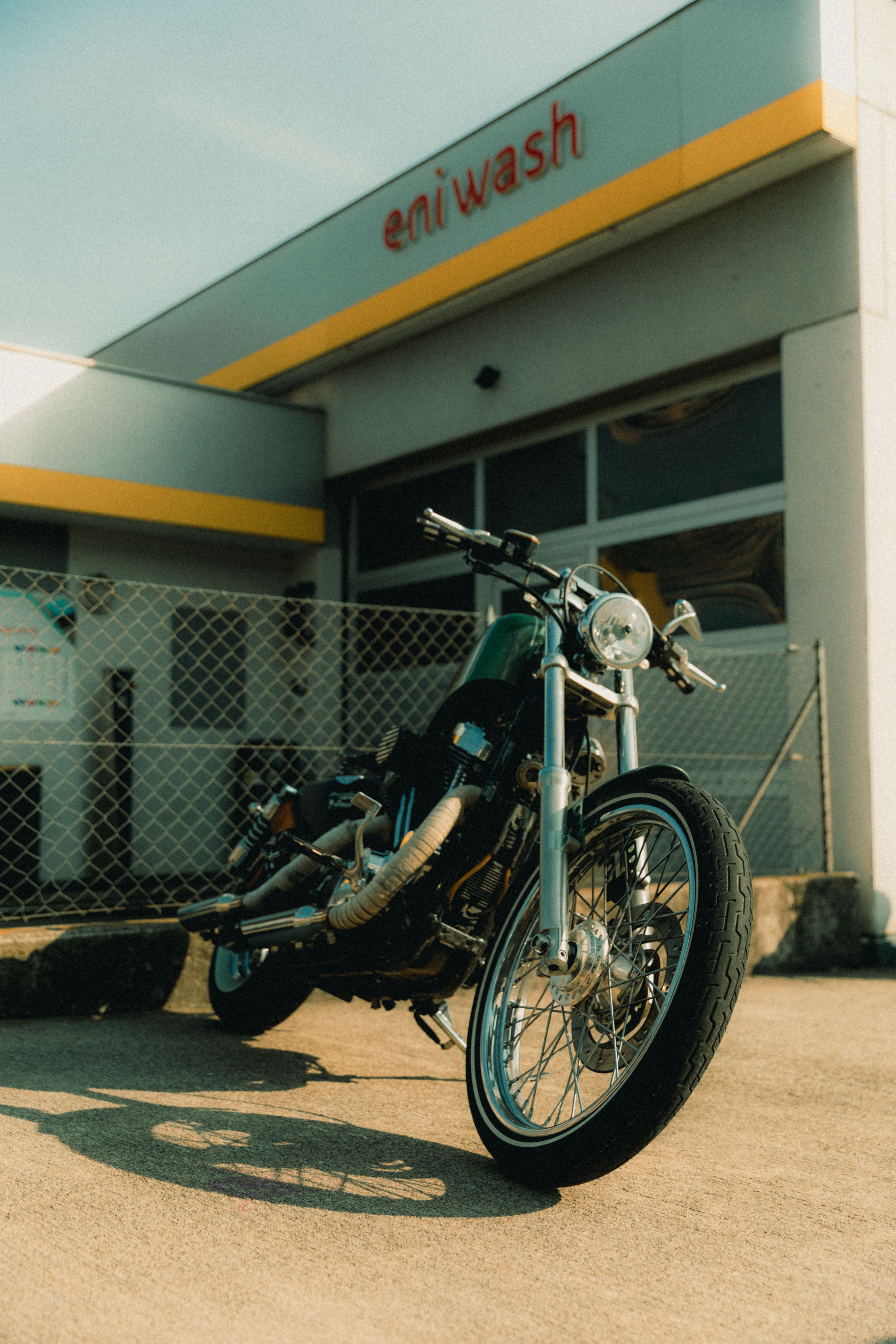 Classic motorcycle parked outside a car wash in Lugano, Switzerland under a clear sky.