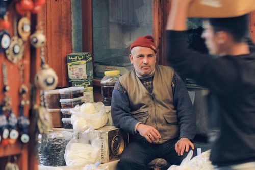 Free A man wearing a hat sits at a traditional market stall surrounded by various goods. Stock Photo