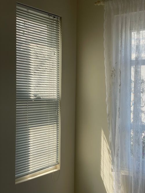 Free Sunlit room corner featuring blinds and a delicate curtain casting shadows. Stock Photo