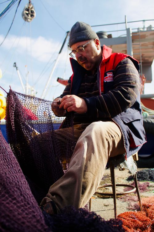 Free A fisherman mending nets at a bustling harbor, capturing the essence of fishing life. Stock Photo