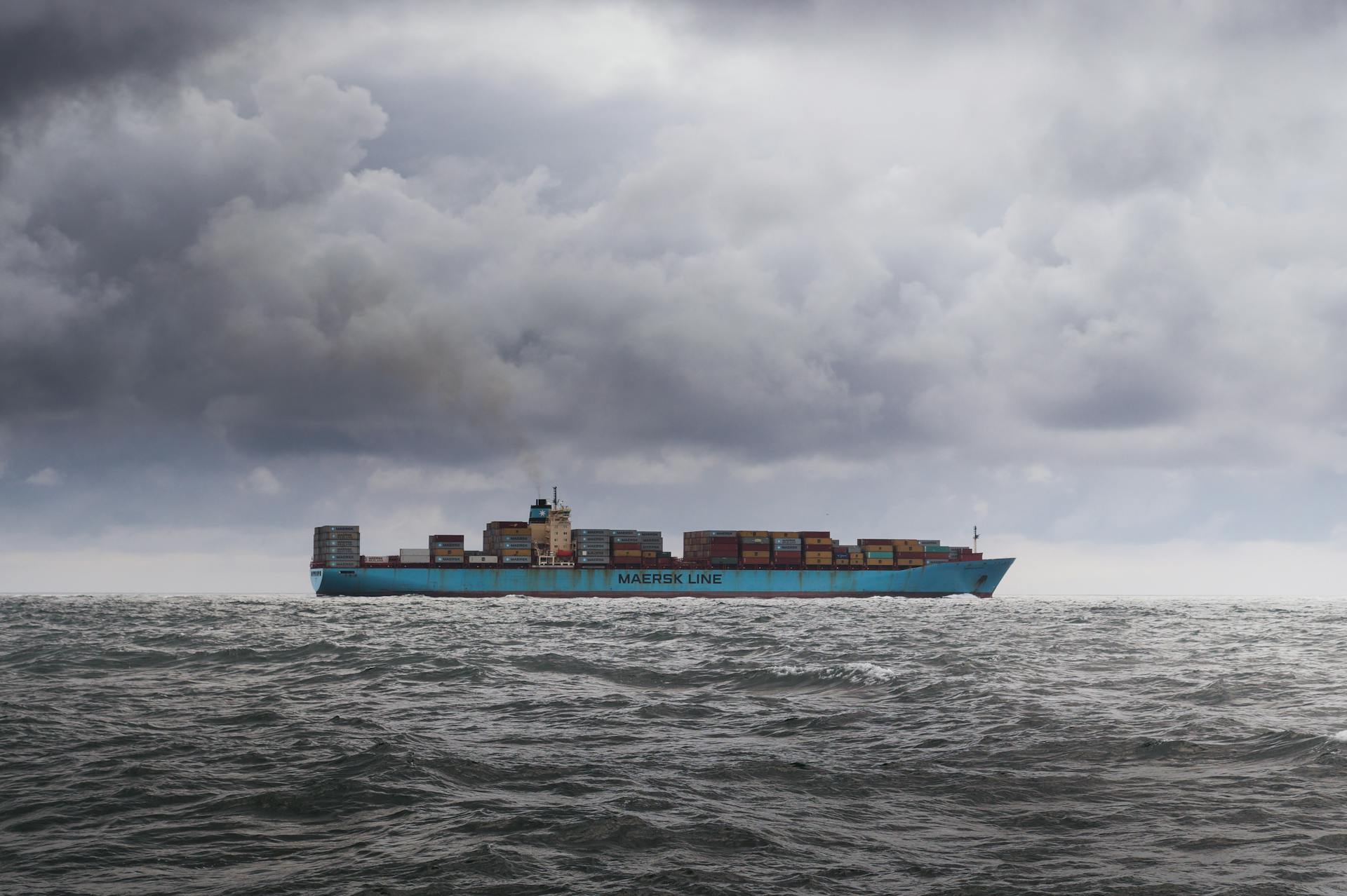 A large cargo ship carrying containers on a cloudy ocean horizon.