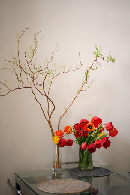 Bright tulips in a glass vase on a table with twigs for elegant home decor.