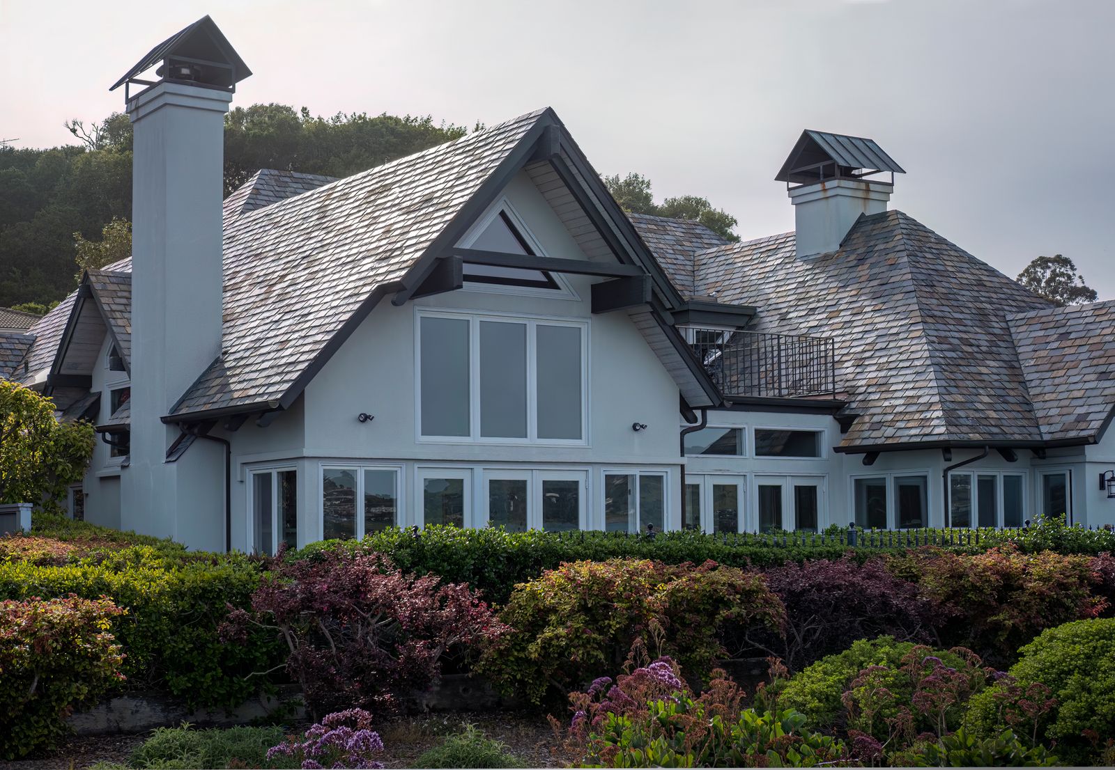 Upscale stately villa with landscaped gardens, a prominent chimney and elegant rooflines