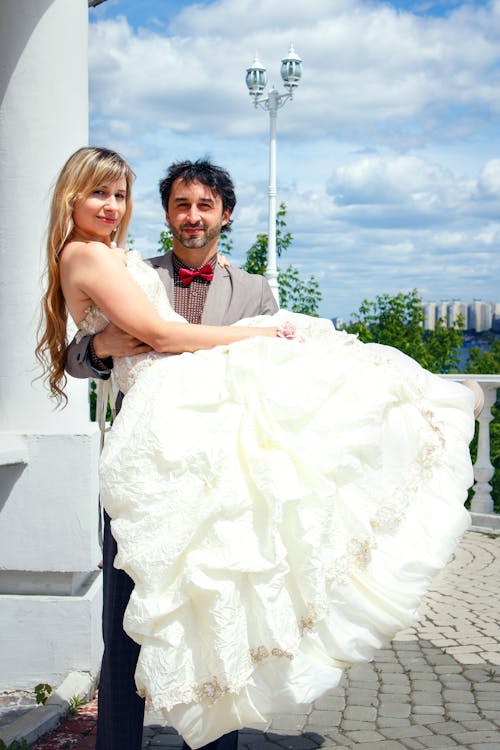 Мужчина несет женщину в белом свадебном платье