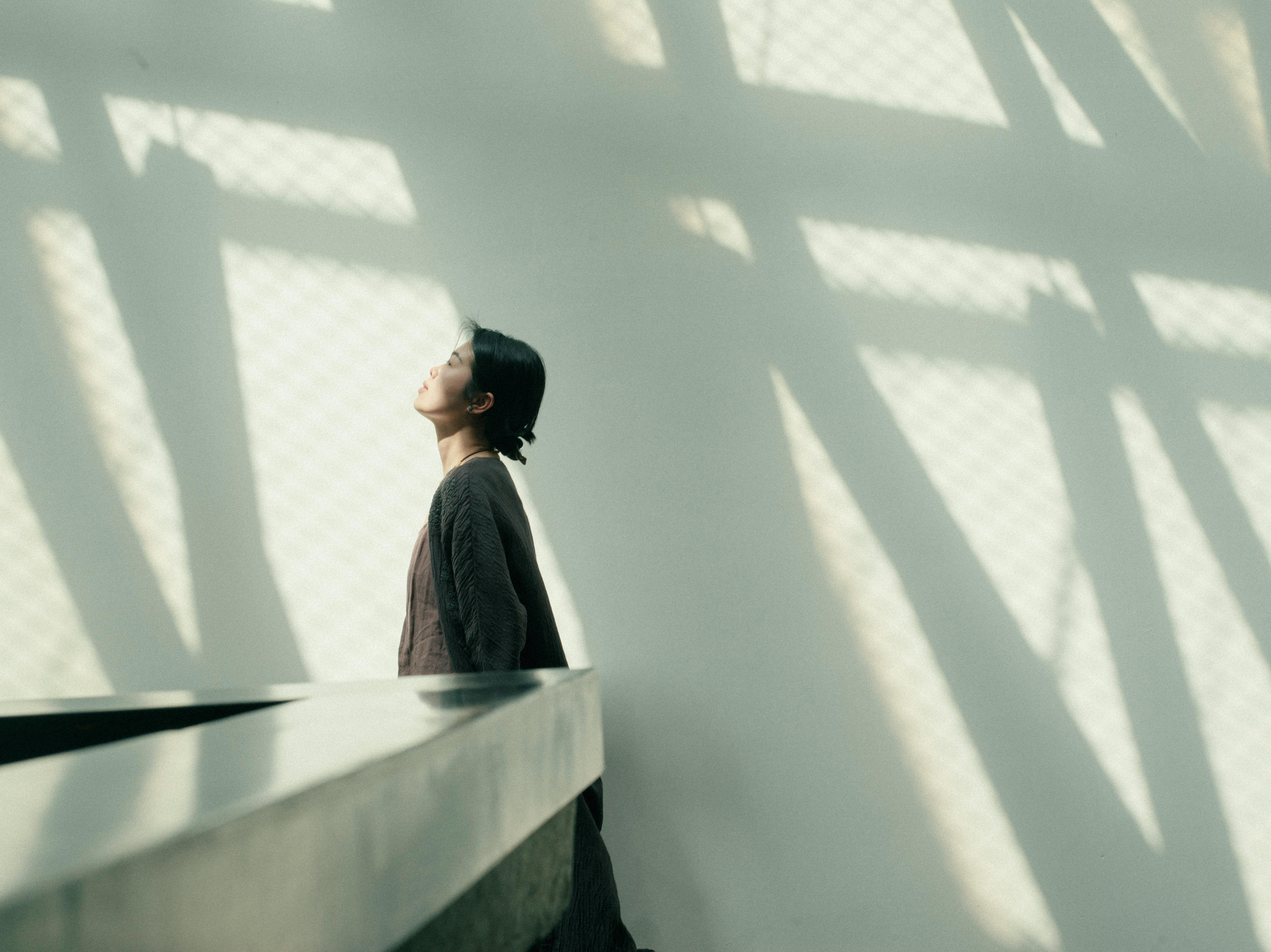 Asian woman standing against white wall with abstract shadows in an urban setting.