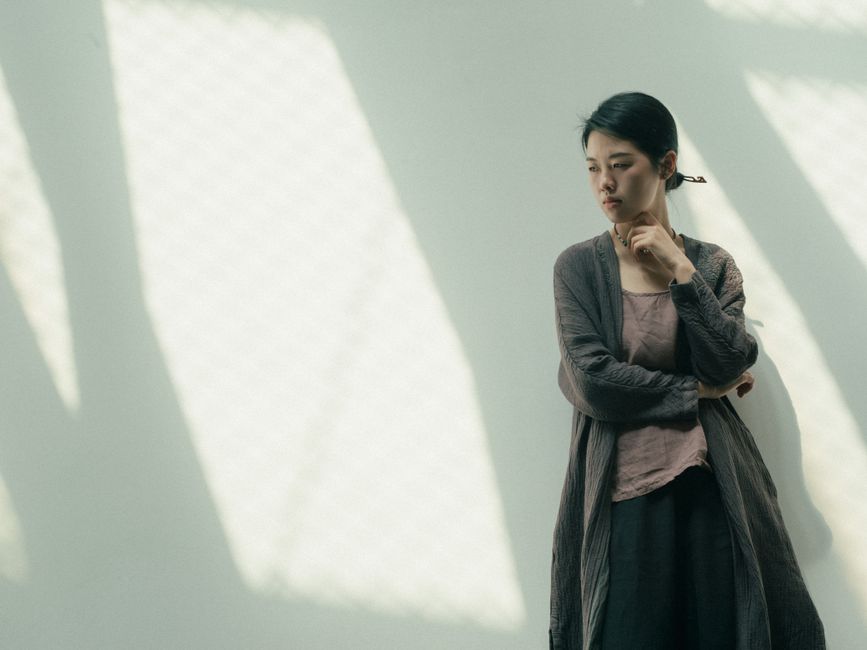 A thoughtful young Asian woman poses against sunlit walls, creating a tranquil and introspective mood.